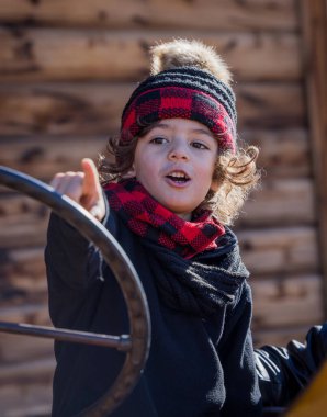 Child in red plaid winter hat and scarf pointing outdoors