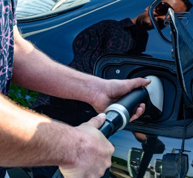 A partial view of a man's hand holding am EV charging cable.