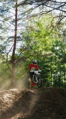 A motorcyclist kicks up dust while riding uphill in a forest