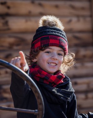 Smiling child in red plaid winter hat and scarf pointing outside