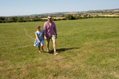 Father and daughter walking hand in hand through a pasture.