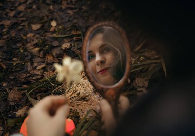 A woman's face in a mirror against the backdrop of an autumn forest