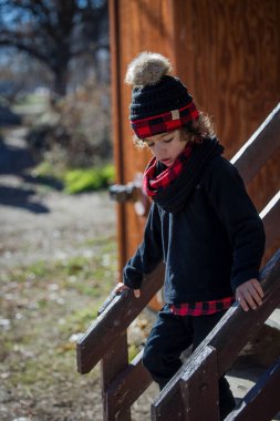 Child in winter hat and scarf walking down wooden steps outdoors