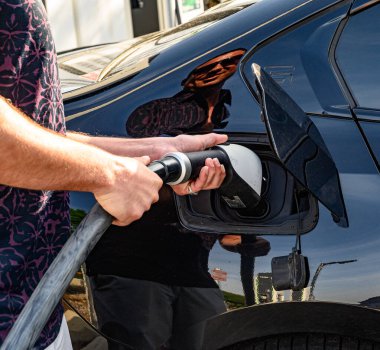 A partial view of a man's hand holding a cable, EV charging station.