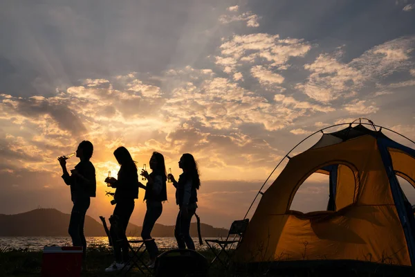 Silhouette Group of teenage asian girl dancing and party with drink bottles happy enjoy travel camping beside the lake at sunset. — Stock Photo, Image
