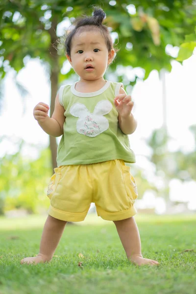 Asian little girl is standing on the lawn at the park, — Stock Photo, Image