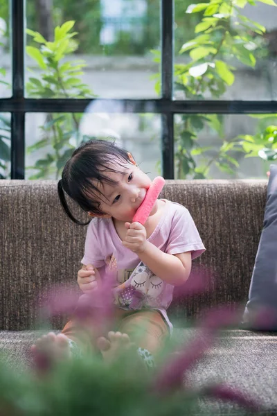 Little asian girl sitting happily eating ice cream sticks in the — Stock Photo, Image