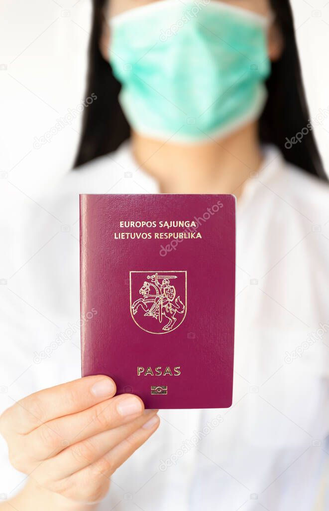 A women with a surgical mask holding Lithuanian passport during Covid 19 outbreak.