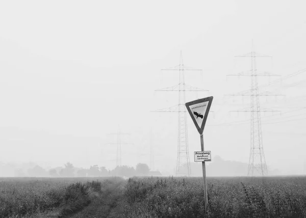 Conservation area sign in front of high-voltage line and field in black an white
