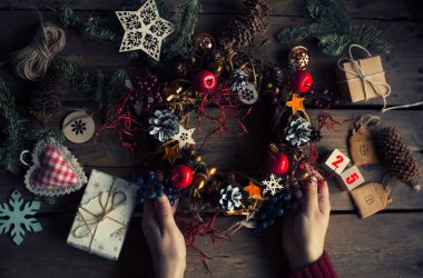 Çam kozalaklı Noel çelengi, meşe palamudu ve sonbahar meyveleri, hediyeler / Noel çelengi yapan kadın elleri