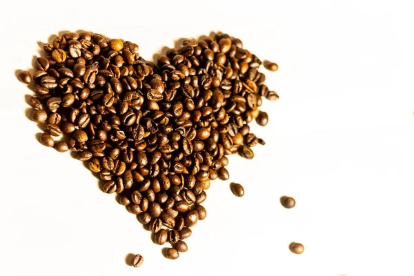 Roasted coffee beans lying in the shape of a heart on a light background