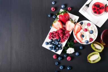 Süzme peynir çilek, yaban mersini ve ahududu beyaz plaka ile kivi, taze sıkılmış meyve suyu ve kek, doğru beslenme