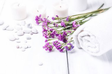 Pembe çiçekler, beyaz çakıl ve beyaz ahşap zemin üzerinde yanan mumlar