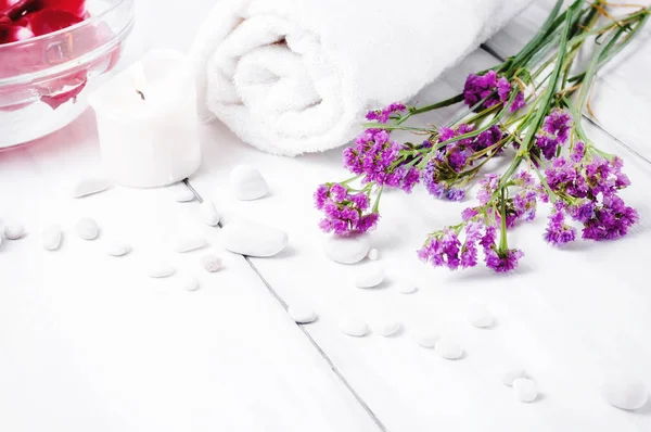 Pembe çiçekler, beyaz çakıl ve beyaz ahşap zemin üzerinde yanan mumlar