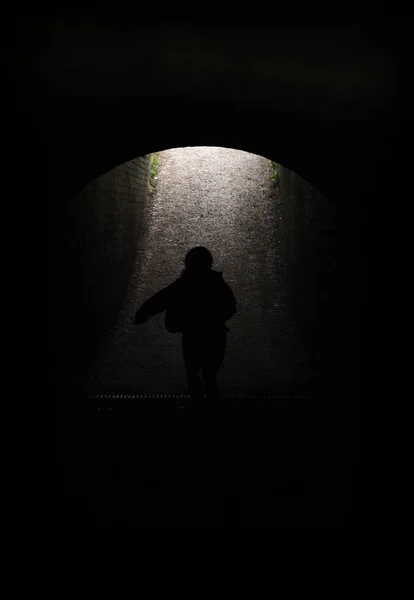 Young child running through a dark tunnel into the daylight