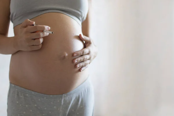 Concept of unhealthy habits during pregnancy. Close up of a pregnant woman smoking cigarette and drinking coffee. toned