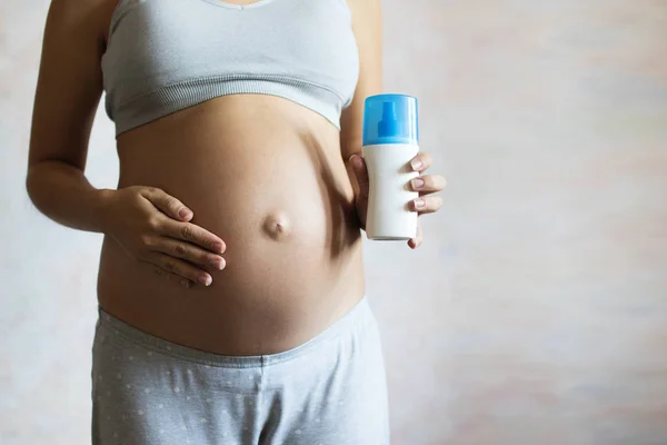 Беременная Женщина Наливает Сливки Руку Перед Нанесением Живот — стоковое фото