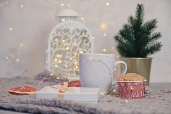 Inverno ainda vida de cachecol, caneca branca de cacau, café ou chocolate quente, muffin, árvore de Natal em xadrez quente com guirlanda . — Fotografia de Stock