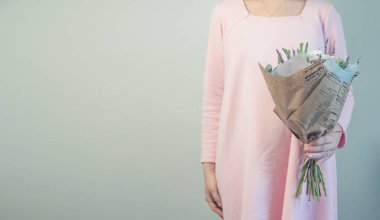 Gri duvar arka plan üzerinde pastel pembe ve krem renklerde çiçekler taze ortanca, eustoma, gül, okaliptüs, lavanta, güzel ihale çiçek buketi tutan çok güzel genç kadın