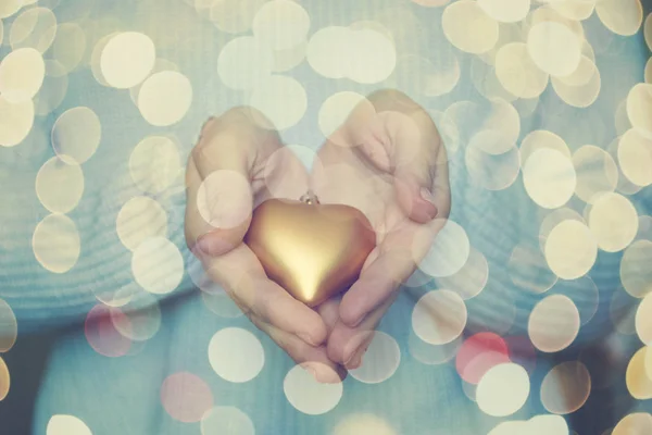 Kadın elele bir kar kış arka planda bir güzel parlak altın kalp. Aşk ve St. Valentine rahat kavramı.