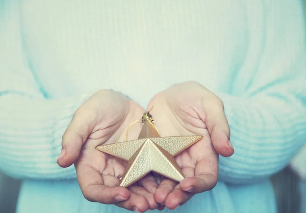 Mãos de mulher estão segurando uma bela estrela de ouro brilhante em um fundo de inverno de neve. Amor e São Valentim conceito acolhedor . — Fotografia de Stock