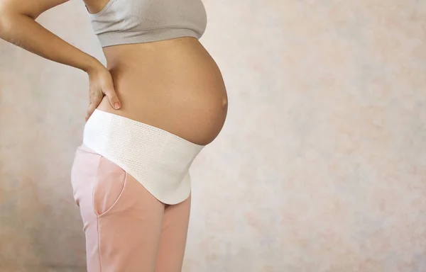 Mulher grávida adorável usando apoio abdominal contra fundo branco — Fotografia de Stock