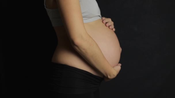 Mulheres grávidas acariciando sua barriga câmera lenta fundo escuro — Vídeo de Stock