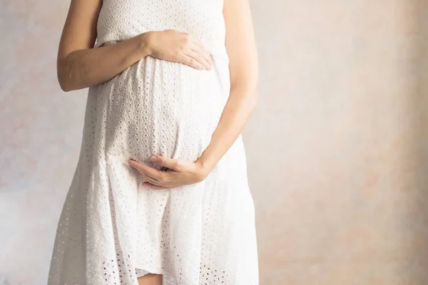 Těhotná žena v šatech drží ruce na břiše na světlém pozadí. Těhotenství, mateřství, přípravu a očekávání koncept. Detail, kopie prostor. Foto krásné nabídku náladu těhotenství. — Stock fotografie