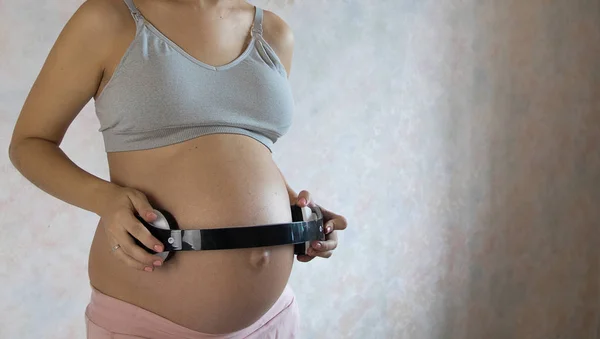Беременная женщина держит наушники на животе на белом фоне — стоковое фото