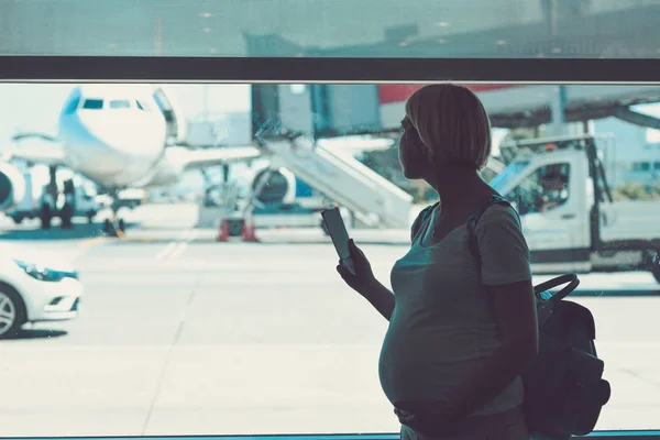 Беременная женщина летит на самолете, стоящем у окна — стоковое фото