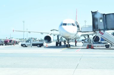 Modern passenger airplane parked to terminal building gate at airside apron of airport with airplane parts jet engine wing windows clipart