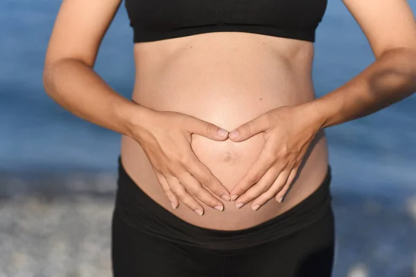 Gravid kvinna beach - händer i hjärtat formen på magen — Stockfoto