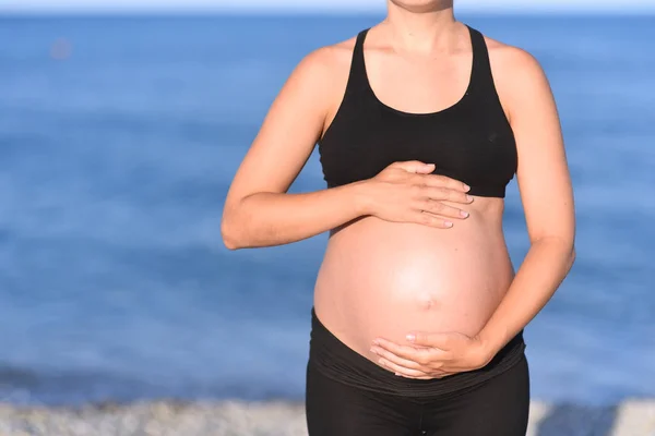 Těhotná žena beach - ruce ve tvaru srdce na břicho — Stock fotografie