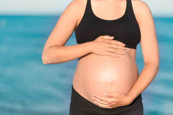 Gravid kvinna beach - händer i hjärtat formen på magen — Stockfoto