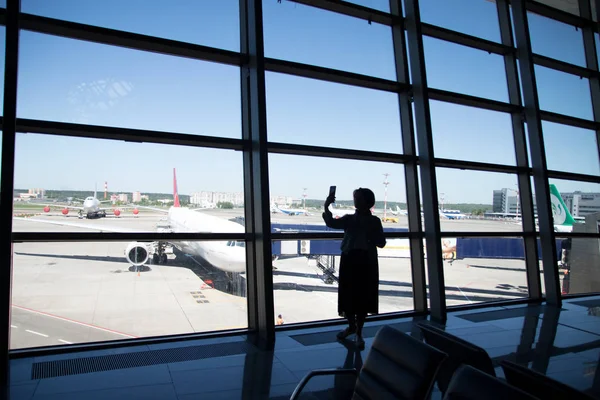 Νεαρή γυναίκα στο αεροδρόμιο, κοιτάζει από το παράθυρο τα αεροπλάνα. — Φωτογραφία Αρχείου