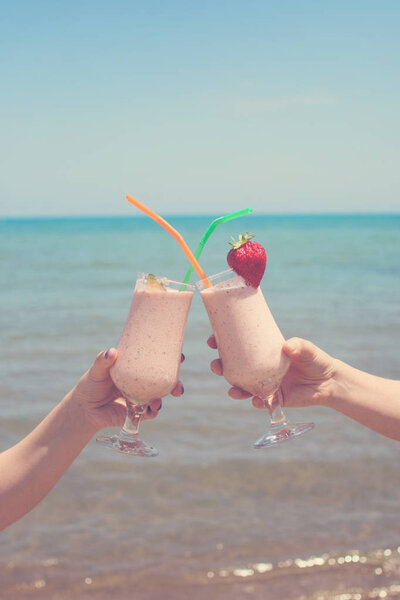 two female hands are holding strawberry milkshakes on the background of the sea