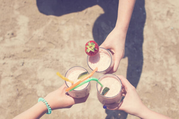 Three female hands are holding strawberry milkshakes on the background of the sea