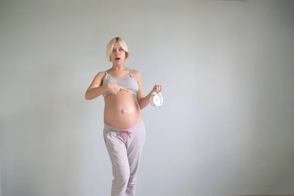 Портрет изумленной беременной женщины с настенными часами — стоковое фото