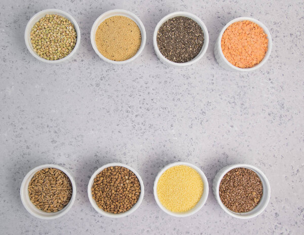 Collection of different groats on grey background. Top view of buckwheat, chia, flax, amaranth, lentils, couscous, wheat