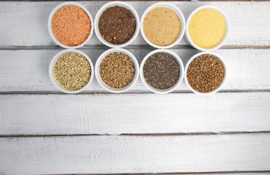 Gri arka plan üzerinde farklı kabuğu çıkarılmış tane topluluğu. Karabuğday, chia, keten, amaranth, mercimek, kuskus, buğday üstten görünüm