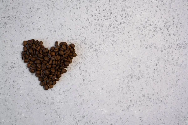 Aceite esencial de café en una botella de vidrio, granos de café en forma de corazón sobre fondo gris — Foto de Stock