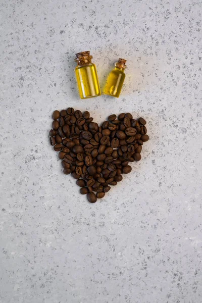 Coffee essential oil in a glass bottle, coffee beans in shape of heart on grey background