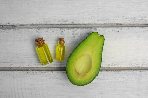 Природные продукты для ухода за кожей. Масло авокадо в бутылках рядом с нарезанным авокадо на сером фоне — стоковое фото