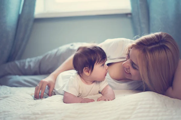 Happy smiling mother and baby lying on bed at home — Stock Photo, Image