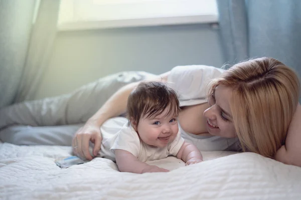 Happy smiling mother and baby lying on bed at home — Stock Photo, Image