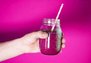 Mans el beyaz duvar arka plan üzerinde Berry Smoothie ile bir cam kavanoz tutarak.