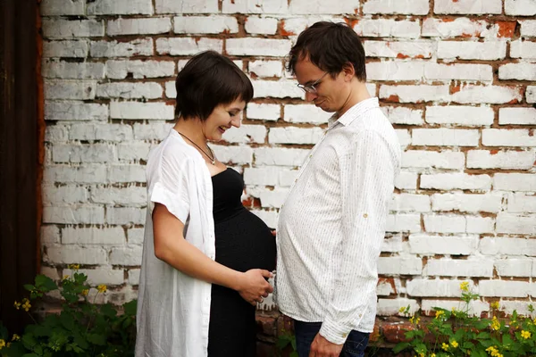 Gravid par jämföra storleken på deras stora mage, moderskap koncept porträtt, på grå bakgrund — Stockfoto