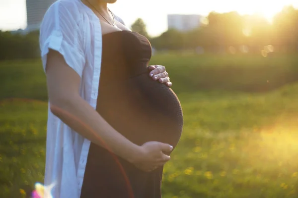Närbild av gravid kvinna är avkopplande i trädgården vid solnedgången. gravid kvinna som håller magen och blomman i trädgården — Stockfoto