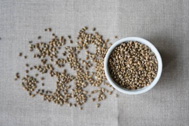 Keten arka plan üzerinde kenevir tohumu dolu beyaz bir seramik kase