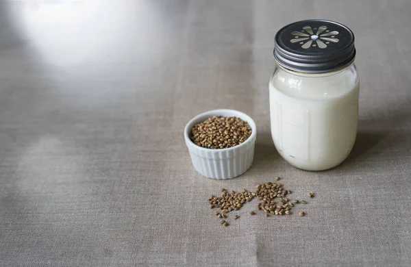 Leche fresca vegana de semillas de cáñamo en un frasco de vidrio, comer limpio, leche no láctea. Fondo de lino — Foto de Stock